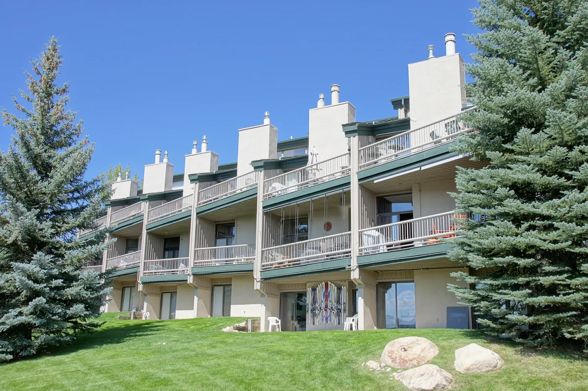 The exterior of the building, with balconies overlooking a green lawn and pine trees. The building’s facade is visible, offering a sense of arrival and outdoor space, while the tranquil setting highlights the natural surroundings.