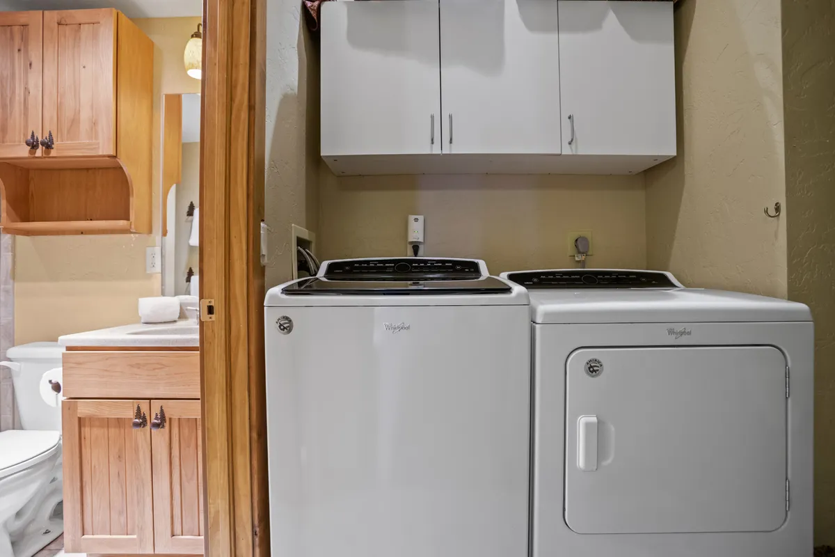 A bright, organized laundry room featuring a modern washing machine and dryer, wood cabinetry for storage, and neatly arranged laundry supplies. The space looks clean, functional, and easy to use for longer stays.