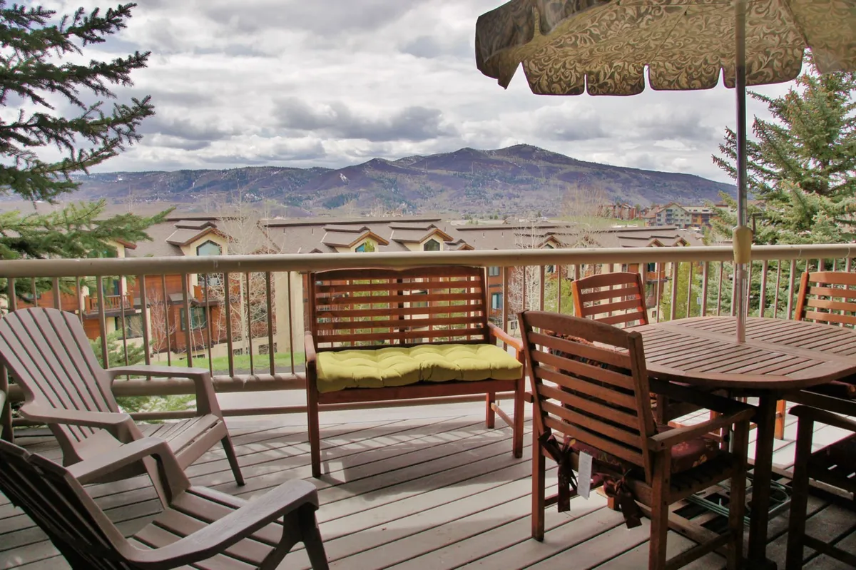 A spacious deck with a wooden dining table and lounge chairs, all oriented toward a breathtaking mountain view. A decorative umbrella adds shade and style, creating a perfect setting for outdoor dining, relaxing, and enjoying the sunrise or sunset.