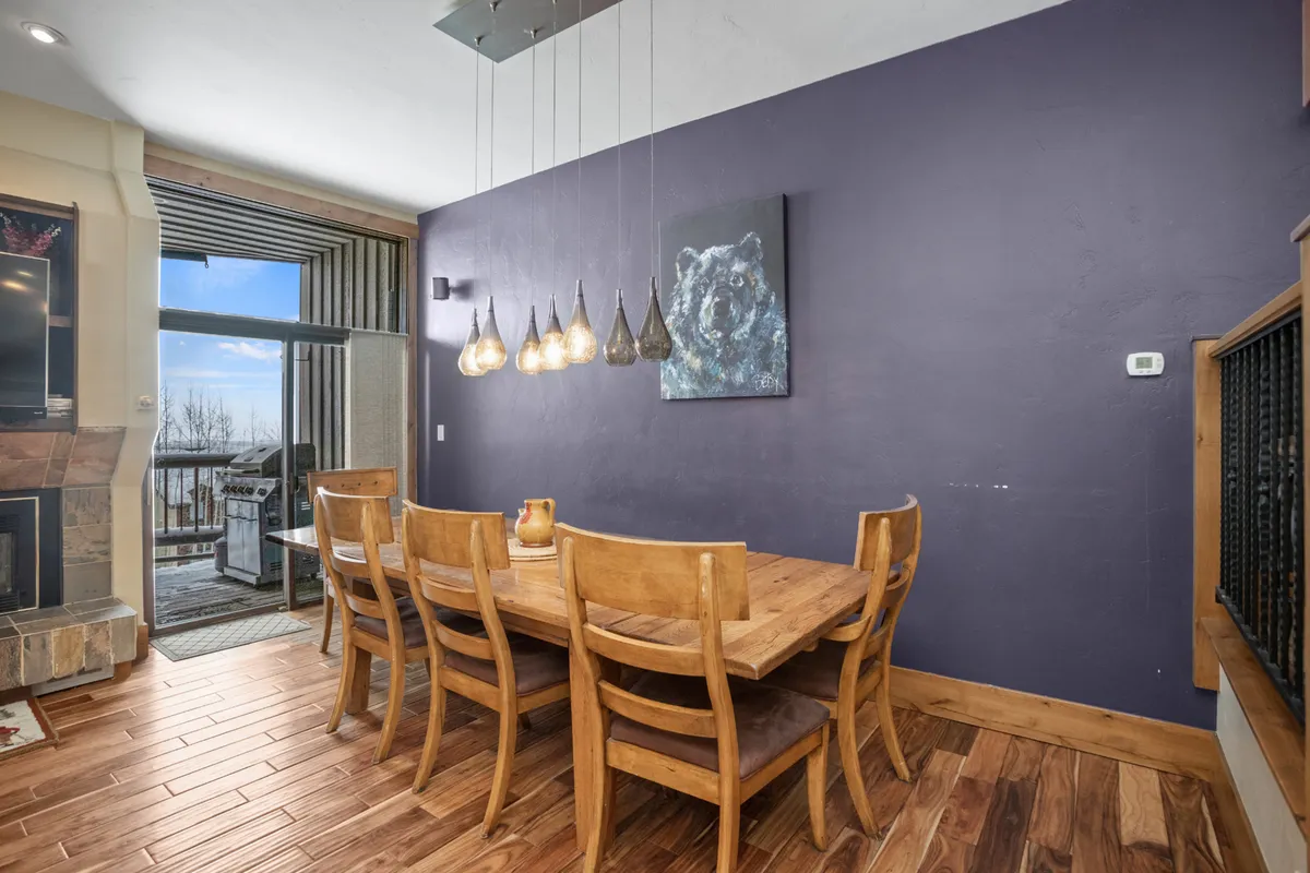 A spacious dining area with a large table, modern pendant lighting, and a distinctive bear painting on the wall. Expansive windows allow in natural light, and the setting is ideal for group meals or intimate gatherings after a day exploring the mountains or downtown.