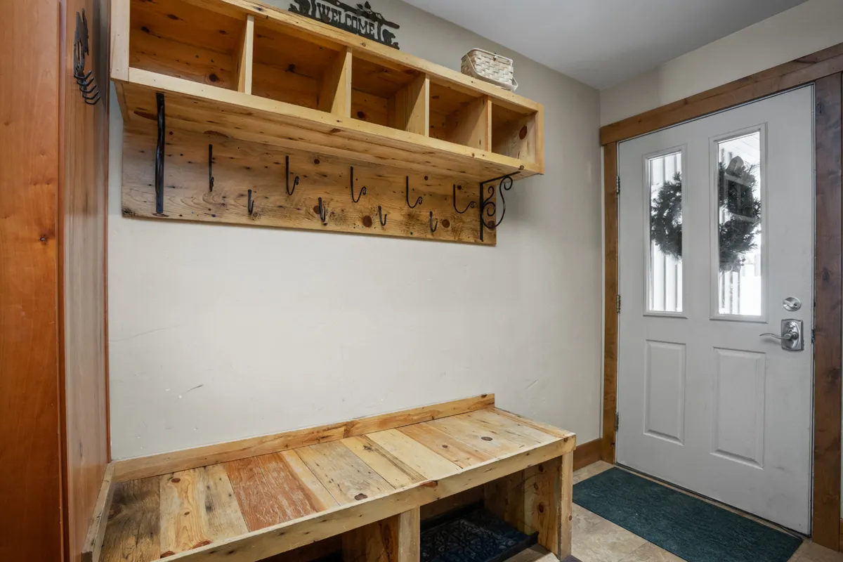 A welcoming entryway with a wooden bench, cubbies, hooks for hanging items, and a front door with glass panels. The space is tidy and thoughtfully organized, providing a glimpse of a well-maintained and secure home environment.