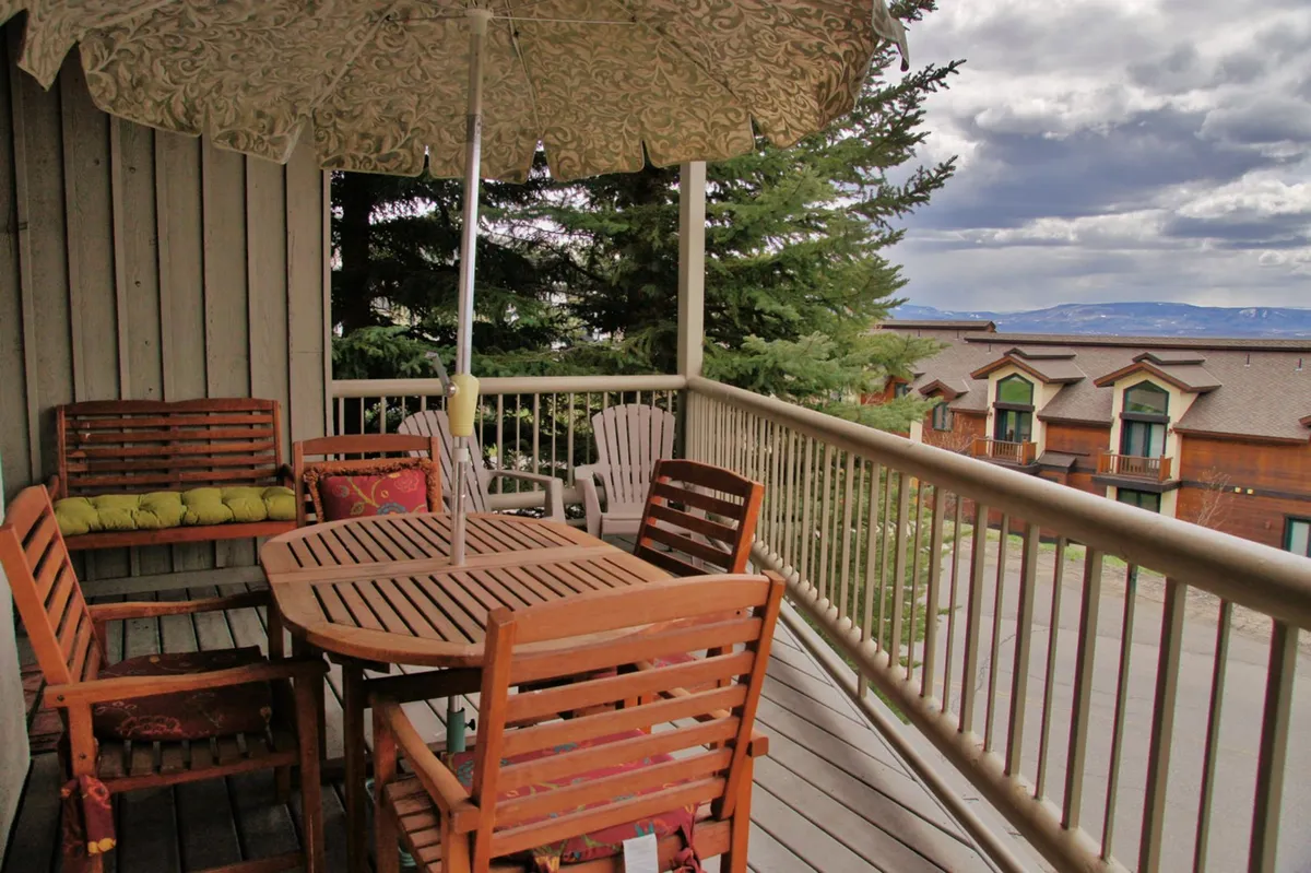 An inviting outdoor dining area with a wooden table, green-cushioned chairs, and a parasol, set against a backdrop of trees. The space feels casual yet comfortable, perfect for savoring sunset views or gathering for outdoor meals.