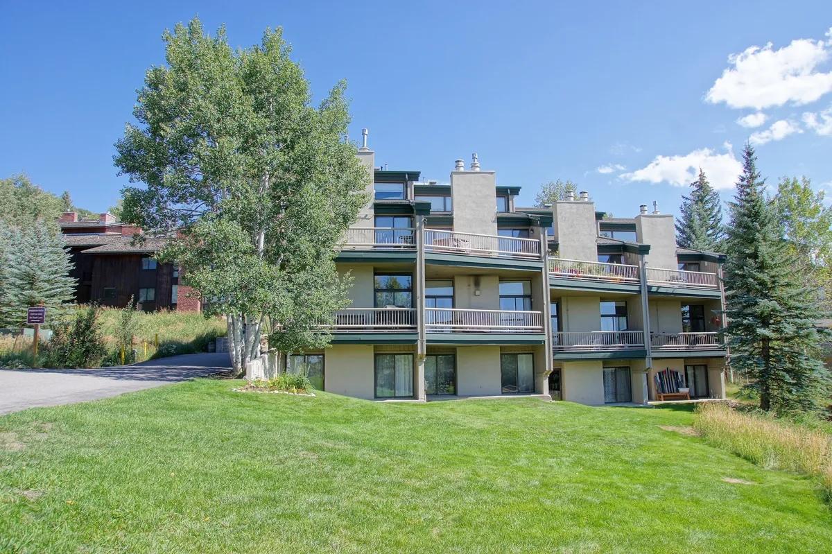 This exterior image features a three-story building set amidst a lush green lawn, with balconies overlooking the surrounding trees. The overall ambiance is tranquil and inviting, suggesting seamless access to nature and outdoor relaxation.