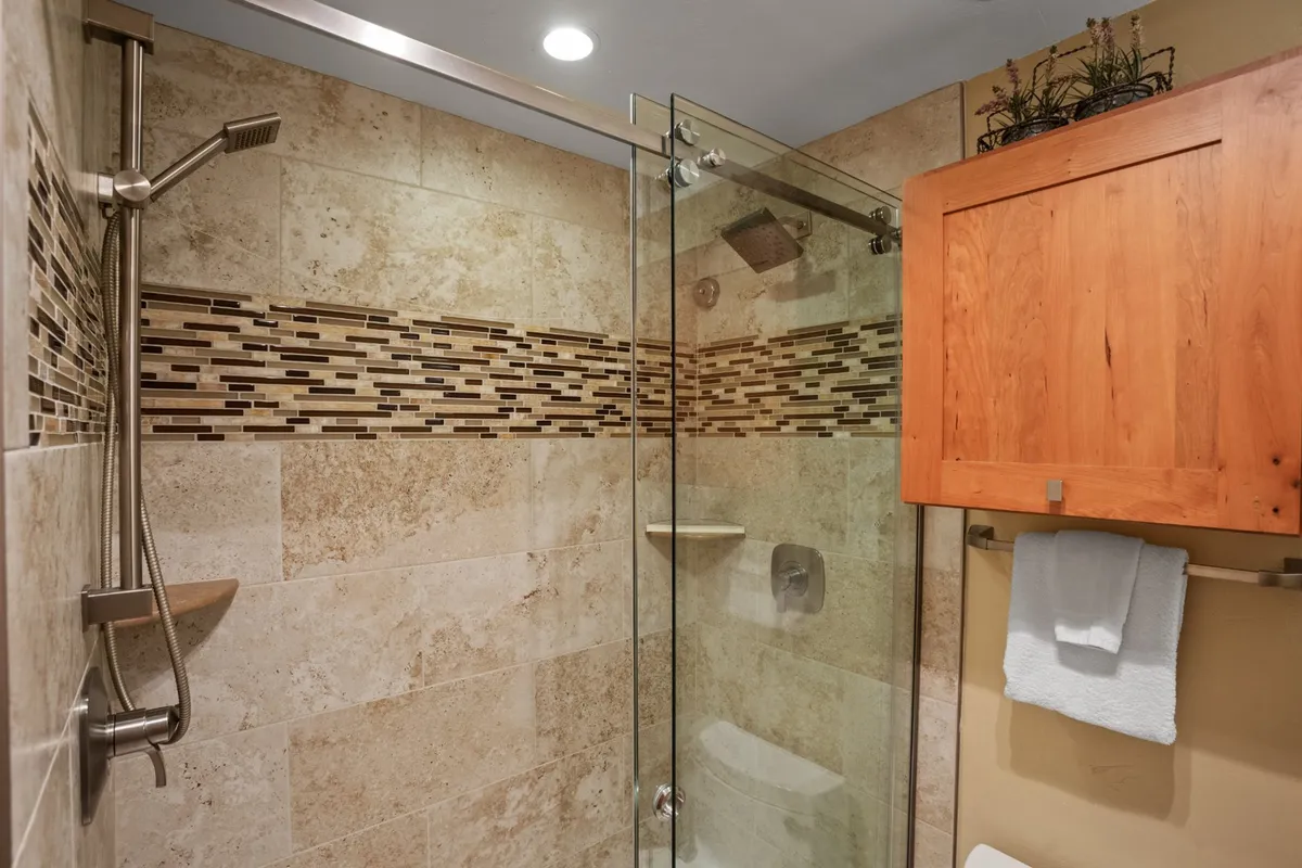 A modern bathroom featuring a glass shower enclosure, textured tile backsplash, and a wooden cabinet. The serene atmosphere and quality finishes hint at a spa-like experience for personal care and relaxation.